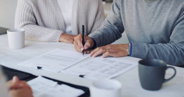 Two people sit at a table, immersed in legal planning for subdividing land in New Zealand. One person signs a paper while the other observes intently. Nearby, cups and additional documents clutter the table, marking the seriousness of their endeavor.